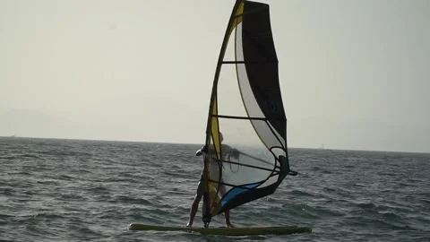 A man sails on a board with a sail at sunset. A man windsurfs Stock Footage 266052338
