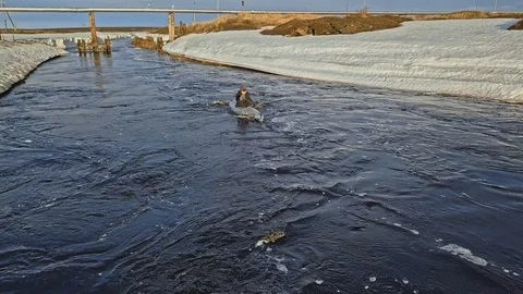Man sails in canoe upstream between frozen river banks Stock Footage 123425914