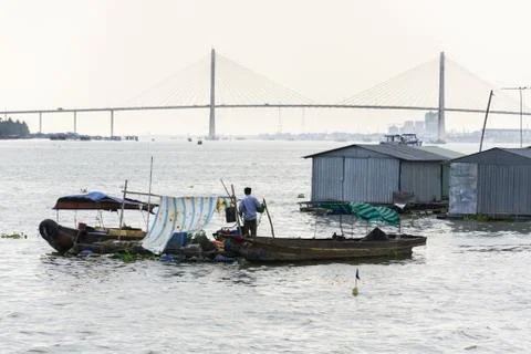 Man sails on ratty boat with fish farm raft houses floating on Mekong river 写真素材