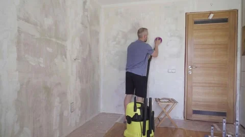 Man sanding interior wall using handheld sander connected to vacuum Stock Footage 330417299