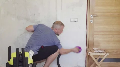Man sands walls before painting using a vacuum to collect dust in a home setting Stock Footage 330417230