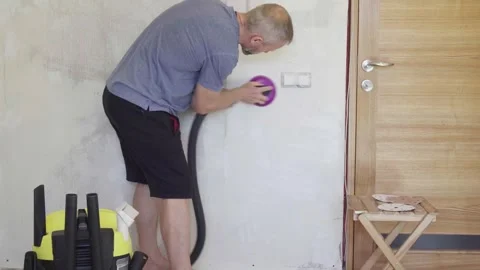 Man sands walls before painting while using a vacuum for dust collection indoors Stock Footage 330417352