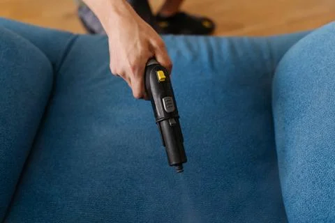 Man sanitizing blue upholstered sofa using powerful steam cleaner, targeting Stock Photos