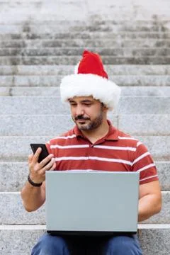 Man with santa claus hat using laptop and smartphone Stock Photos