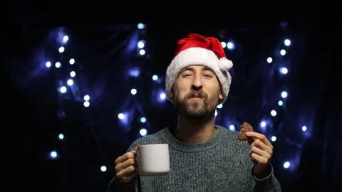 A man in a Santa hat on a bokeh background eats a chocolate cookie with cocoa Stock Footage 142125301
