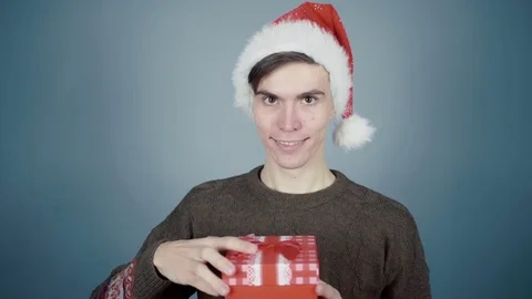 Man in Santa hat opening gift box unexpectedly hand from a box clicks it on nose Stock Footage 70223933