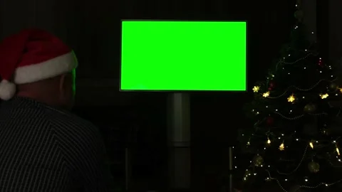Man in Santa hat watching green screen TV on black background on Christmas Video stock 220051564
