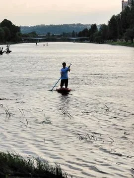 A man on a SAP floats down the river in the evening, steering an oar Stock Photos