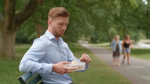 Man Sat On Bench Eats Lunch and Experiences Heart Burn Stock Footage 92560969