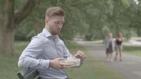 Man Sat On Bench Eats Lunch and Experiences Heart Burn - Ungraded Stock Footage 92561164