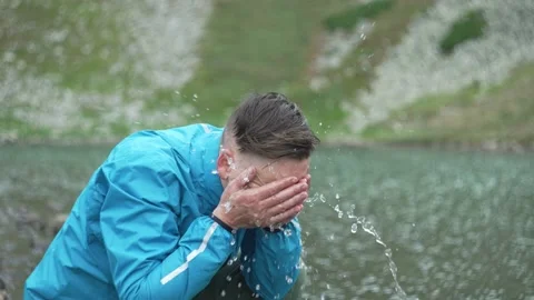 The man sat down on the shore of the lake to wash his face. Water splashes Stock Footage 218441697