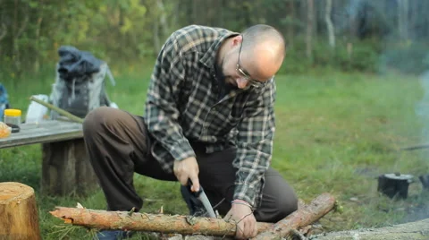 Man sawing a small tree camp saw. Near lit a fire and lay the tourist stuff Video stock 64441085