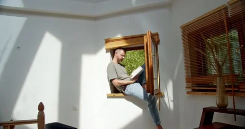 Man in a Scandinavian interior is reading a book sitting on a windowsill with an Vídeo Stock 159485227
