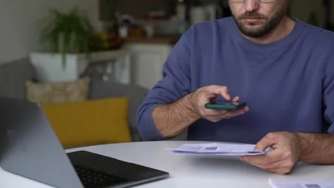 Man scanning QR code on utility bill with smartphone at home for online payment Stock Footage 307224903
