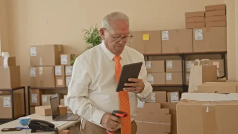 Man scans parcel with handheld scanner while holding a tablet amid stacked .. Video stock 339199360