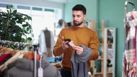 Man scans QR code and label of sweater using mobile phone camera. Stock Footage 327693902