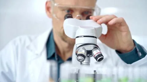 Man scientist with protective glasses using microscope in laboratory Stock Photos
