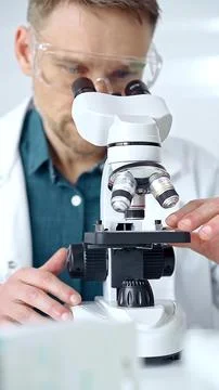 Man scientist with protective glasses using microscope in laboratory Stock Photos