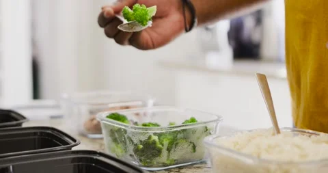Man scooping steamed broccoli with metal spoon into black meal trays on stone Stock Footage 345065240