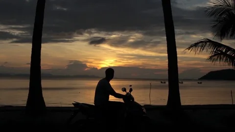 Man on a scooter on the beach with palm trees at sunset Video stock 85280919