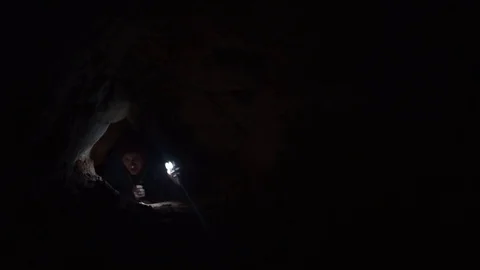 Man scrambles in cave hole illuminates way with flashlight in his smartphone Stock Footage 80053532