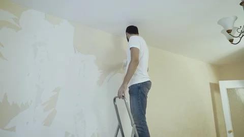 Man in with a scraper on ladder in the process of removing wallpaper. Stock Footage 119563704