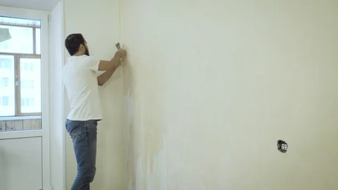Man in with a scraper in the process of removing old wallpaper. Stock Footage 119562910