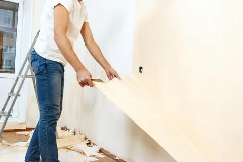 Man in with a scraper in the process of removing old wallpaper. Stock Photos