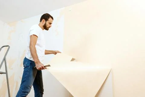 Man in with a scraper in the process of removing old wallpaper. Stock Photos