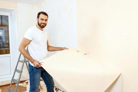 Man in with a scraper in the process of removing old wallpaper. Stock Photos