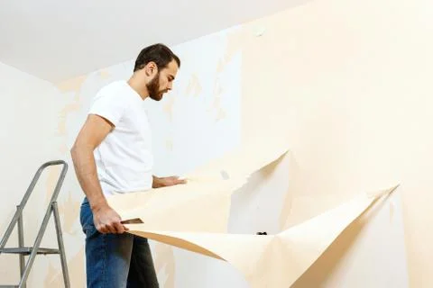 Man in with a scraper in the process of removing old wallpaper. Stock Photos