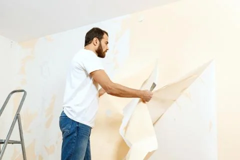 Man in with a scraper in the process of removing old wallpaper. Stock Photos