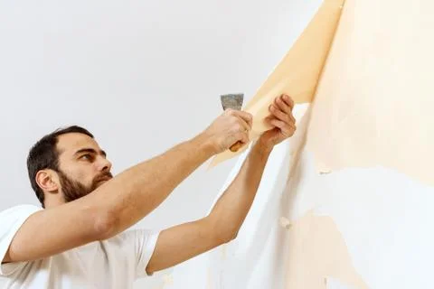 Man in with a scraper in the process of removing old wallpaper. Stock Photos