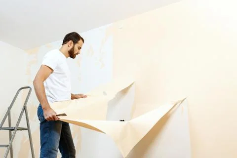 Man in with a scraper in the process of removing old wallpaper. Stock Photos