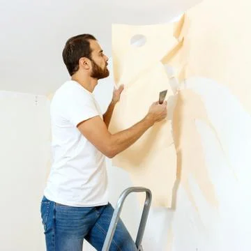 Man in with a scraper in the process of removing old wallpaper. Stock Photos