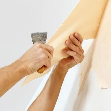 Man in with a scraper in the process of removing old wallpaper. Stock Photos