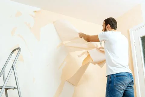 Man in with a scraper in the process of removing old wallpaper. Stock Photos