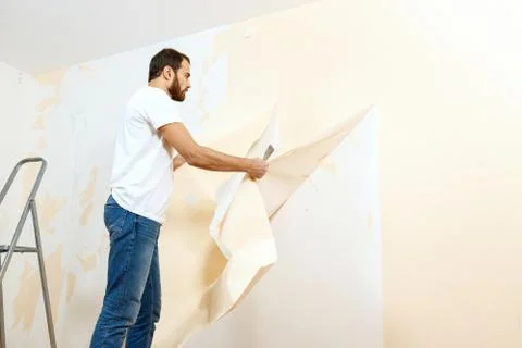 Man in with a scraper in the process of removing old wallpaper. Stock Photos