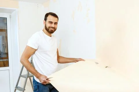 Man in with a scraper in the process of removing old wallpaper. Stock Photos