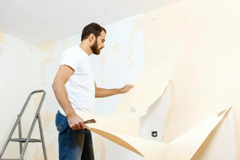 Man in with a scraper in the process of removing old wallpaper. Stock Photos
