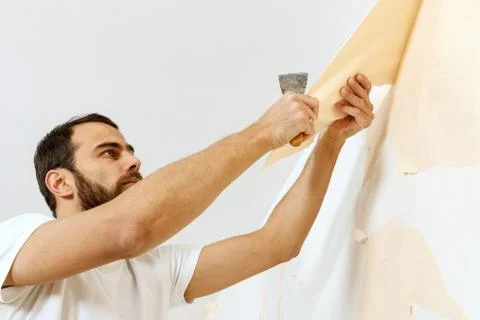 Man in with a scraper in the process of removing old wallpaper. Stock Photos