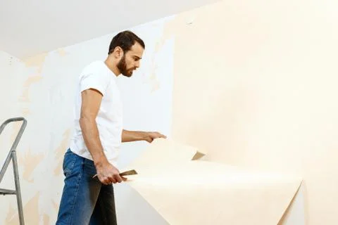 Man in with a scraper in the process of removing old wallpaper. Stock Photos