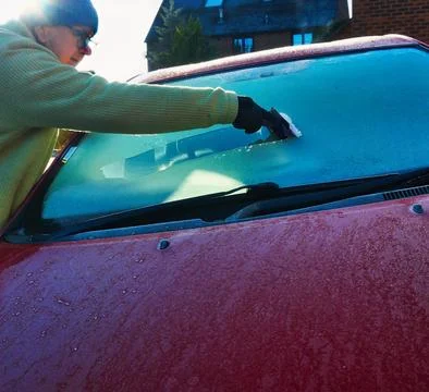 Man scrapes ice to remove ice from car windshield on a cold winter morning 写真素材