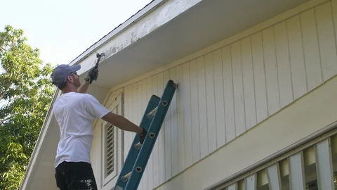 Man Scrapes side of House before Using Paint Sprayer Stock Footage 96881197