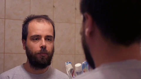 Man scratching his beard in the bathroom mirror Stock Footage 129627064