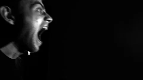 The man screams on a black background in low key, in slow motion, anger emotions Stock Footage