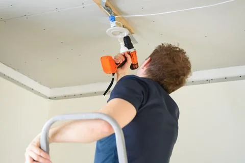 A man with a screwdriver fixes wiring for ceiling lights Stock Photos