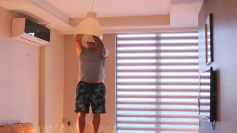 Man screwing light bulb into ceiling lamp housing, installing lighting fixture Stock Footage 333578553