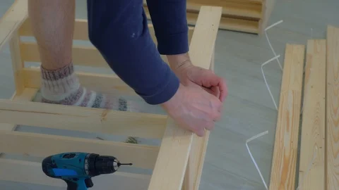 Man screws boards using electric screwdriver collecting rack furniture bookcase. Video stock 129590497