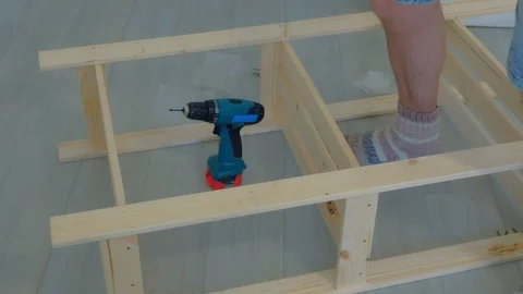 Man screws boards using electric screwdriver collecting rack furniture bookcase. Stock-Footage 129590662